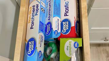 A drawer containing various office supplies including non-stick parchment paper, heavy-duty aluminum foil, plastic wrap, and sandwich bags.