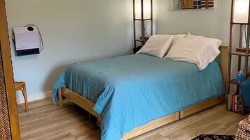 A bedroom with a bed, a standing lamp, a wall-mounted heater, and a decorative rug.