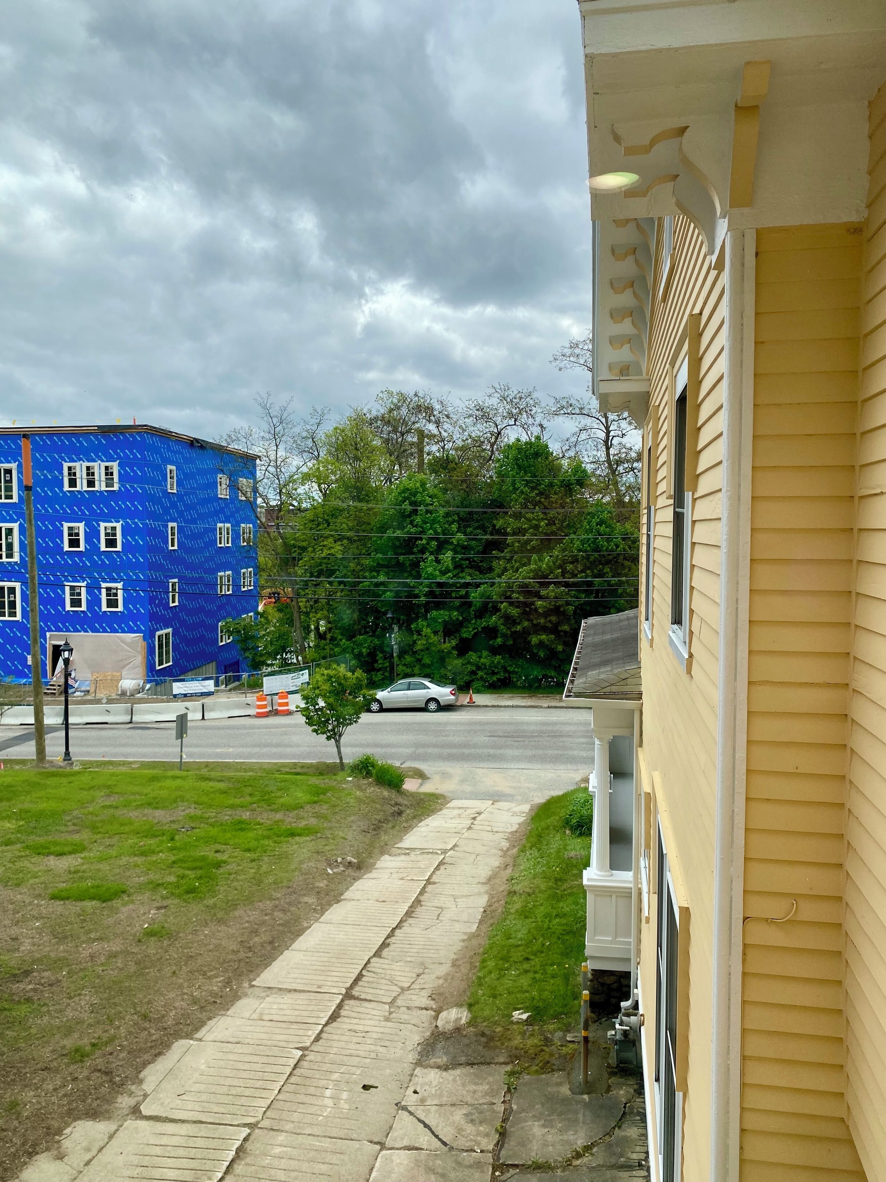 Eine Wohnstraße mit einem gelben Haus, einem blau farbigen Gebäude im Bau und einem Bürgersteig.