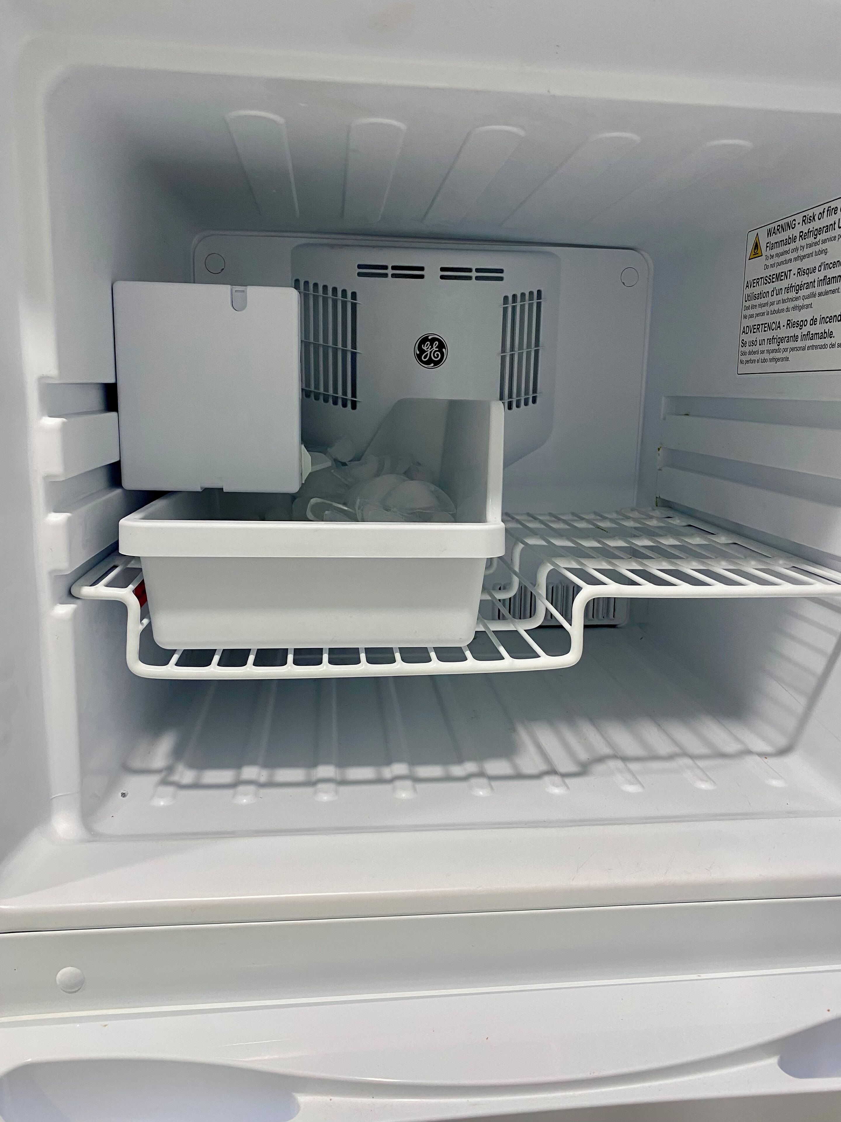 An empty refrigerator with a GE logo, a water and ice dispenser, and a note on the door warning about the risk of fire and the use of flammable refrigerants.