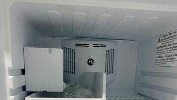 An empty refrigerator with a GE logo, a water and ice dispenser, and a note on the door warning about the risk of fire and the use of flammable refrigerants.