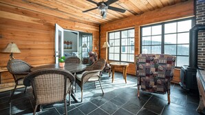 Un intérieur en bois comprenant un coin repas, des chaises en osier, un ventilateur de plafond et de grandes fenêtres.