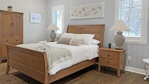 Une chambre à coucher bien rangée, avec un lit en bois, deux tables de chevet avec des lampes, une armoire et une fenêtre avec des stores.