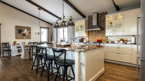 Une cuisine moderne dotée d’un grand îlot central, de meubles blancs et d’un mur d’accent en briques.