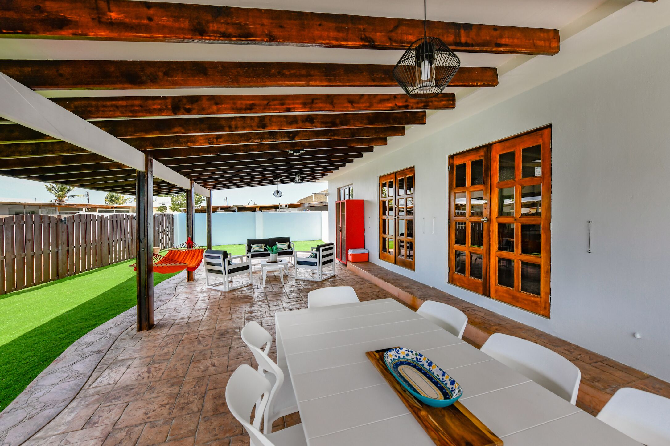 An outdoor patio with a white table and chairs, a hammock, and a view of a backyard.