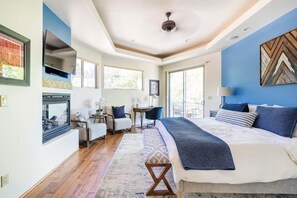 A modern bedroom with a large bed, a fireplace, a desk, and a view of the outdoors.