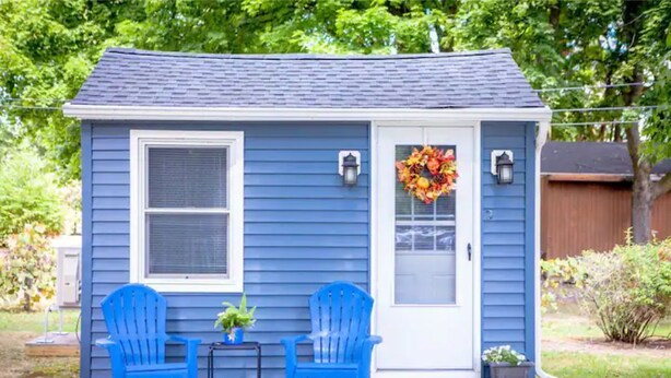 A small blue house with two blue Adirondack chairs, a small table, and a potted plant.