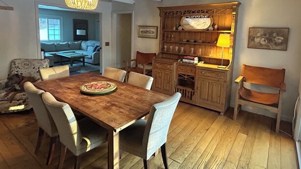 Een eethoek met een houten tafel en stoelen, een kroonluchter en een houten kast met een spiegel en planken.