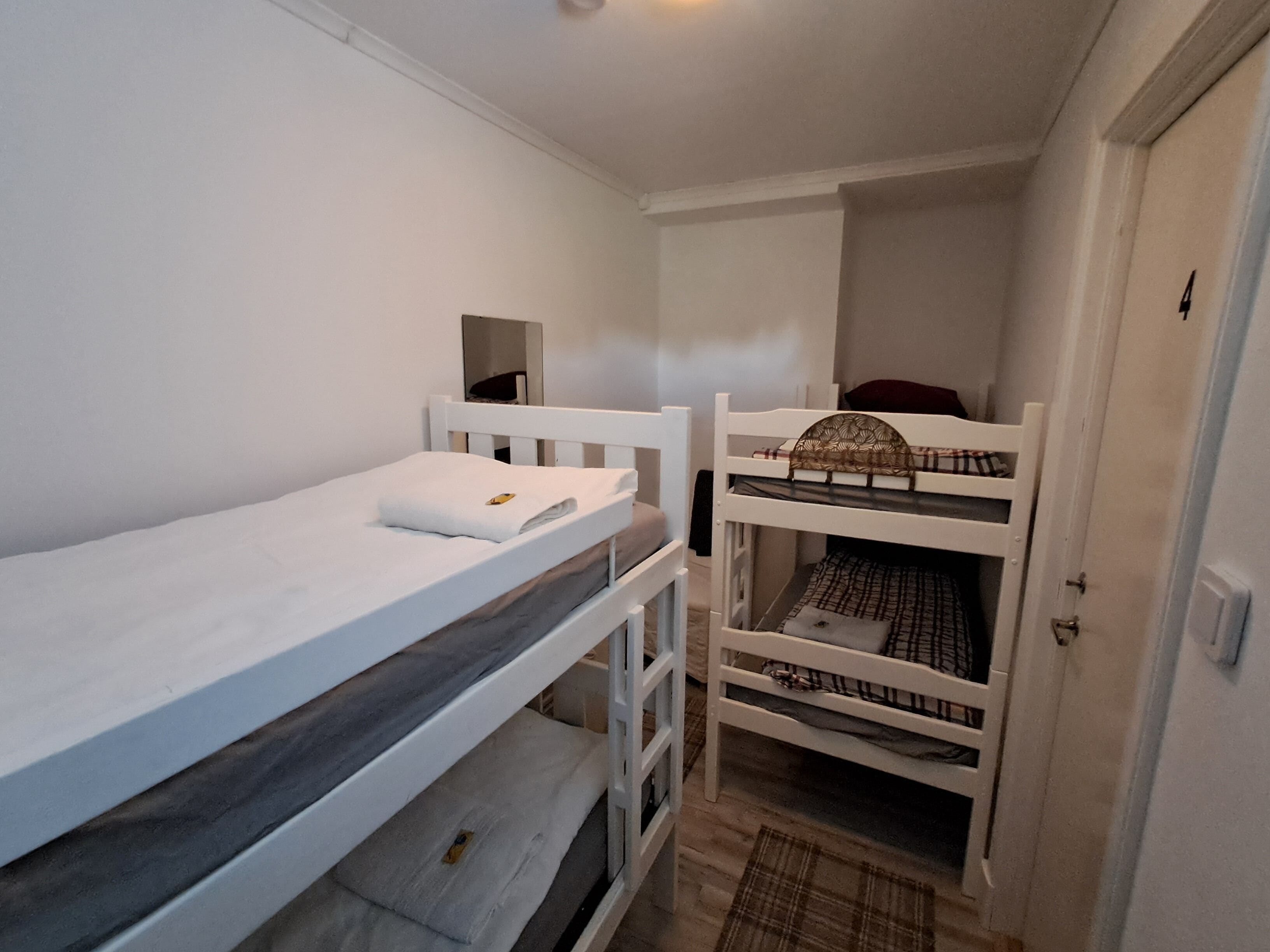 Ett litet, smalt rum med två våningssängar, en vit dörr och en spegel på väggen.