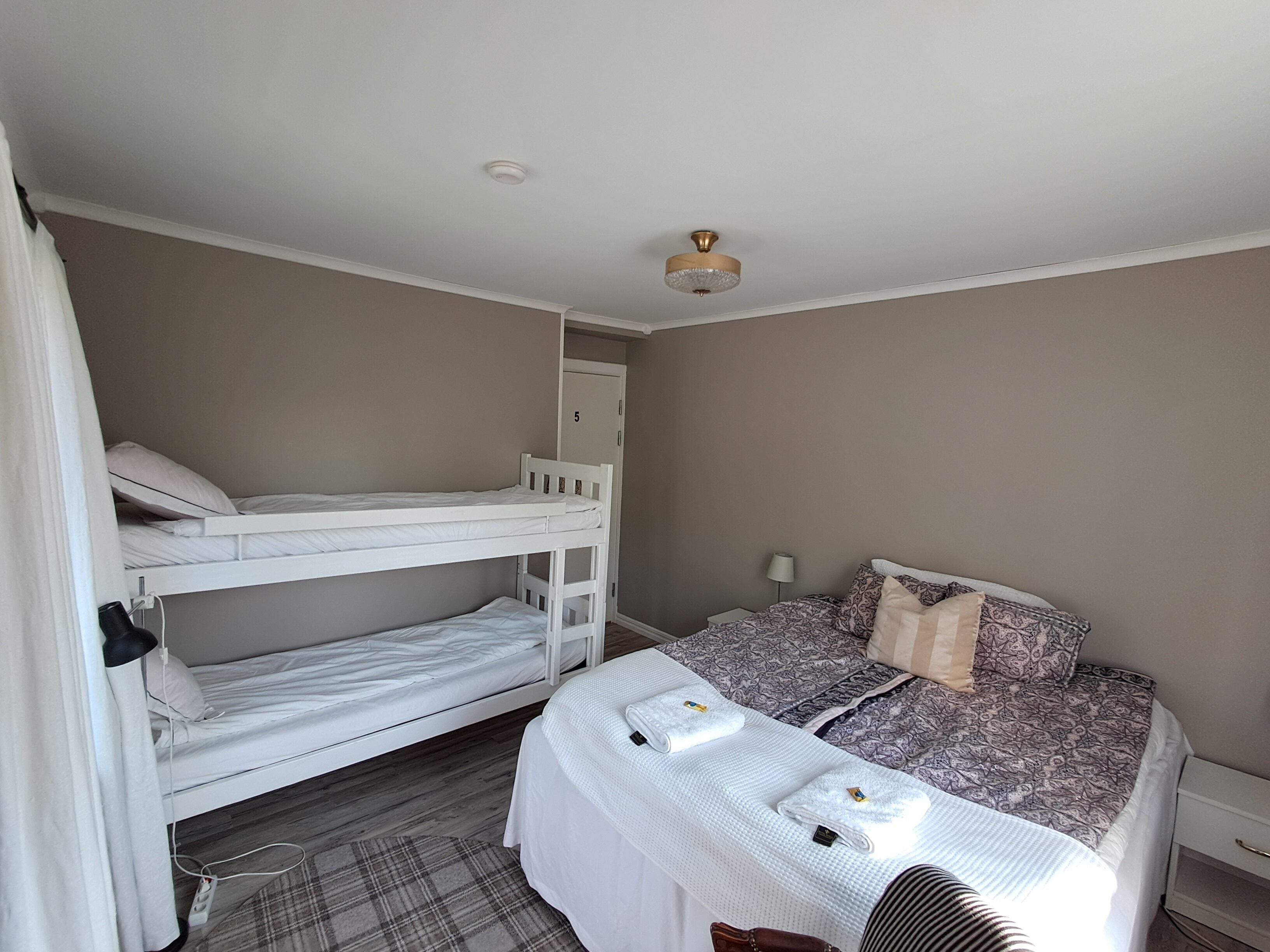 Une chambre avec des lits superposés, un lit simple avec une literie à motifs, une table de chevet et une commode.