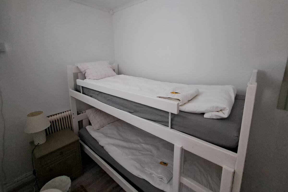 Dormitorio con literas, ropa de cama blanca y una mesita de noche pequeña con lámpara.