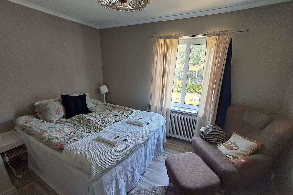 Un dormitorio con cama, una silla, una ventana con cortinas y un radiador.