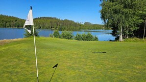 A golf course with a flagstick, a flag, and a golf club on the grass. - Ankis Bed and Breakfast (Storebro)