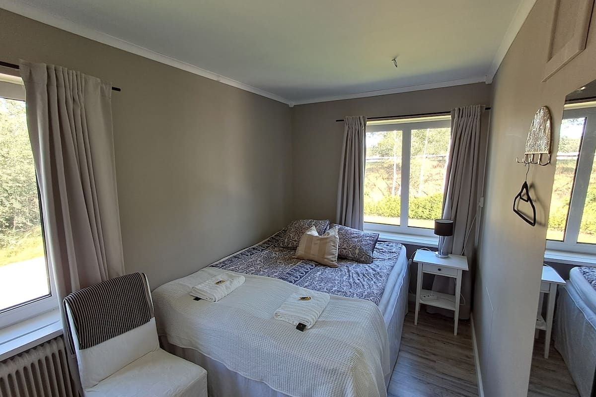 Un dormitorio con una cama grande, una mesita de noche, una silla y una ventana con cortinas.