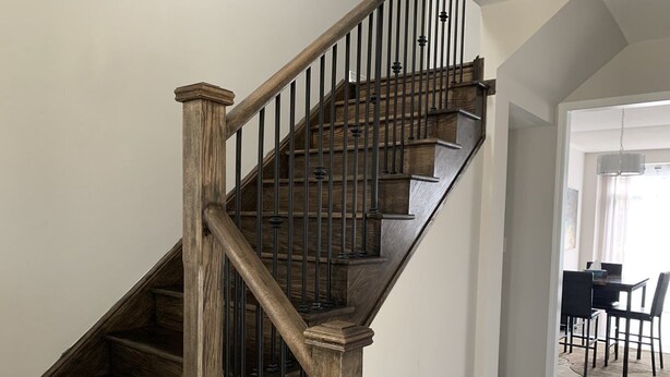 A wooden staircase with a dark finish and metal balusters, leading to a dining area with a table and chairs. - Spacious and modern townhome in Collingwood (Collingwood)