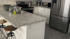 A modern kitchen with white cabinets, a stainless steel refrigerator, a built-in oven, a coffee maker, and a sink. - Spacious and modern townhome in Collingwood (Collingwood)