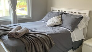 A neatly made bed with grey bedding, a white headboard, and a window with curtains. - Spacious and modern townhome in Collingwood (Collingwood)
