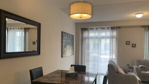 A dining area with a glass-top table, chairs, a hanging light fixture, a large mirror, and a painting on the wall. - Spacious and modern townhome in Collingwood (Collingwood)