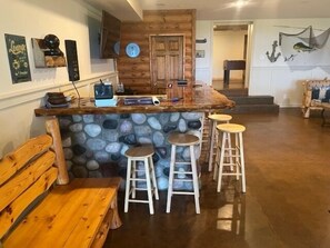 A rustic kitchen with a stone island, wooden stools, and a bench.