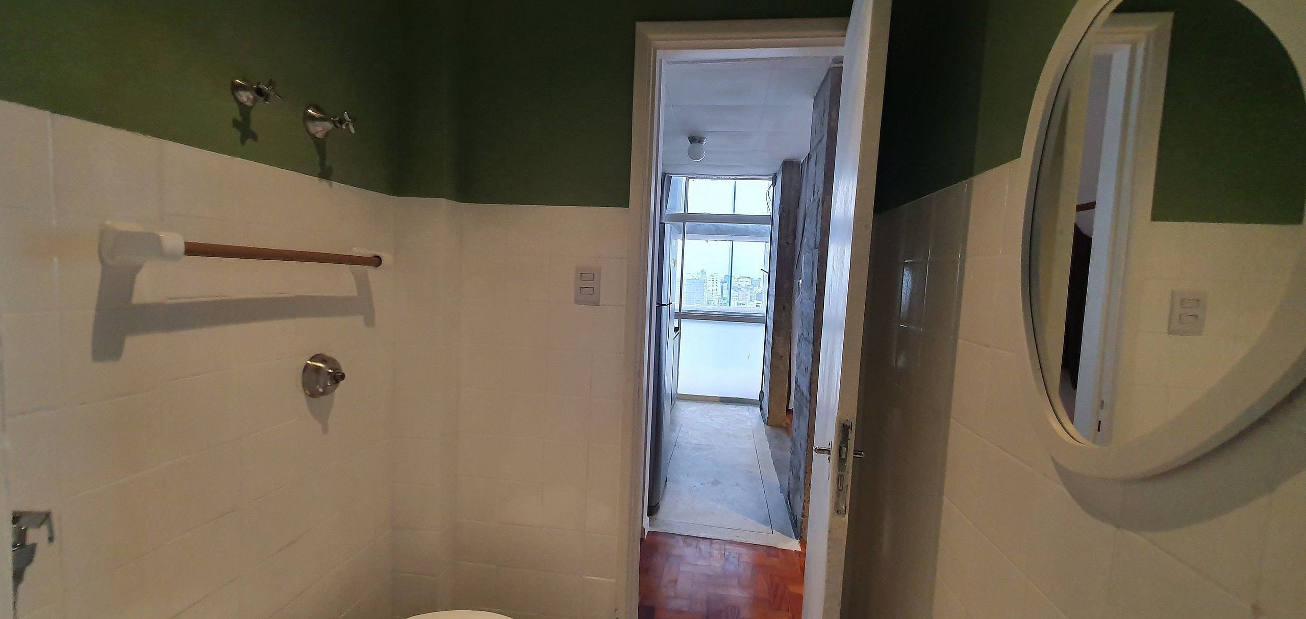 A bathroom with a white toilet, a wooden towel rack, a mirror, and a door leading to a hallway.