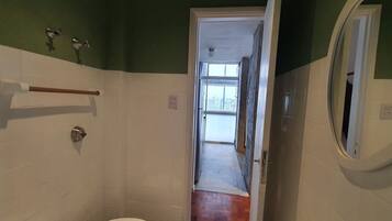 A bathroom with a white toilet, a wooden towel rack, a mirror, and a door leading to a hallway.