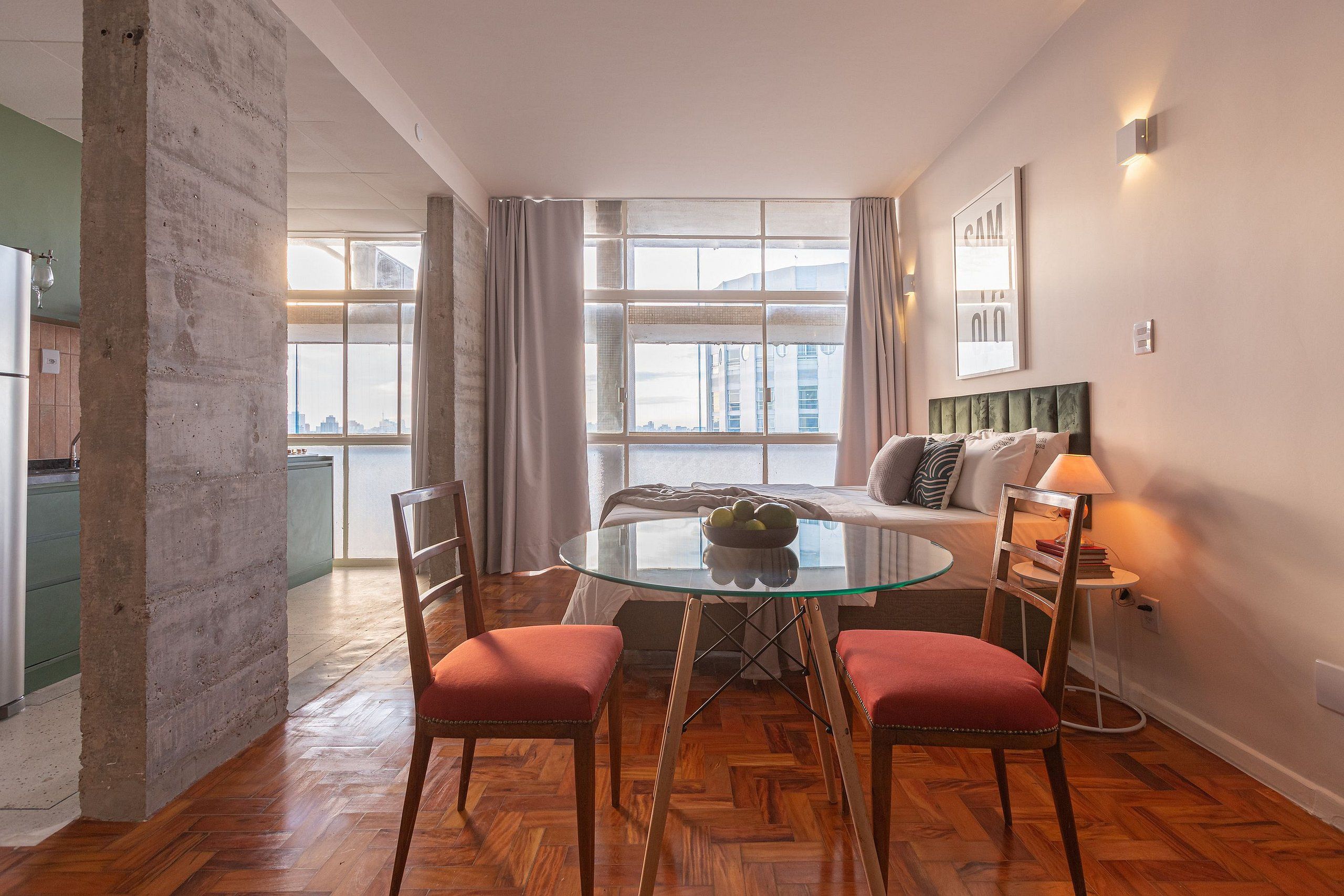 A modern living room with a glass table, wooden chairs, a sofa, and a city view through large windows.