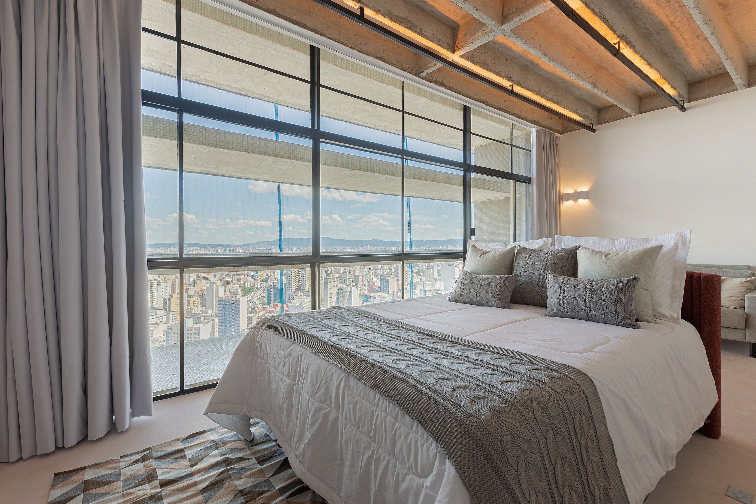 Ein Schlafzimmer mit einem großen Bett, Blick auf die Stadt und einem modernen Deckenstil.