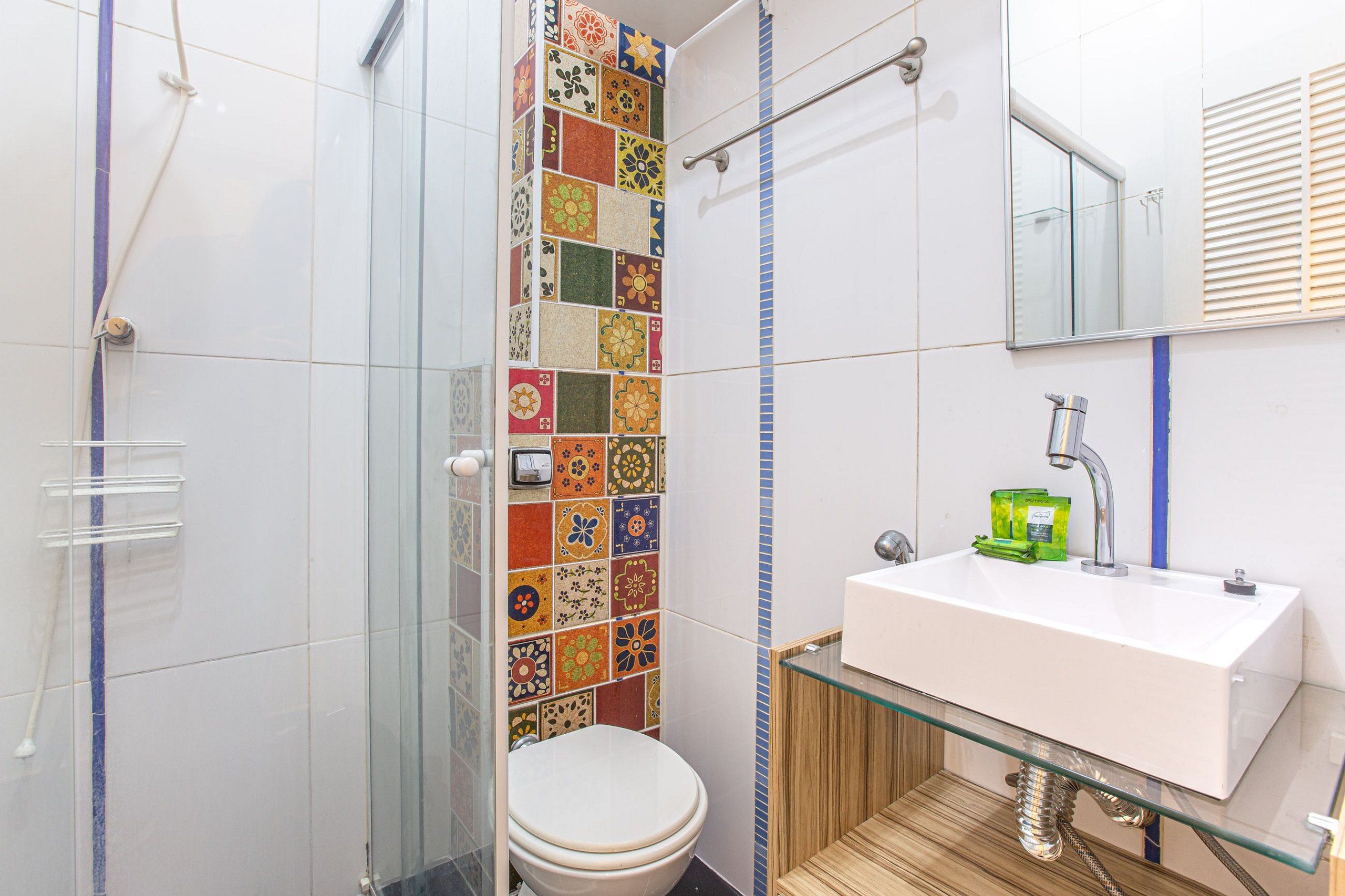 Ein Badezimmer mit Duschkabine aus Glas, einem weißen Waschbecken und einem grünen Seifenspender sowie einer gefliesten Duschwand.