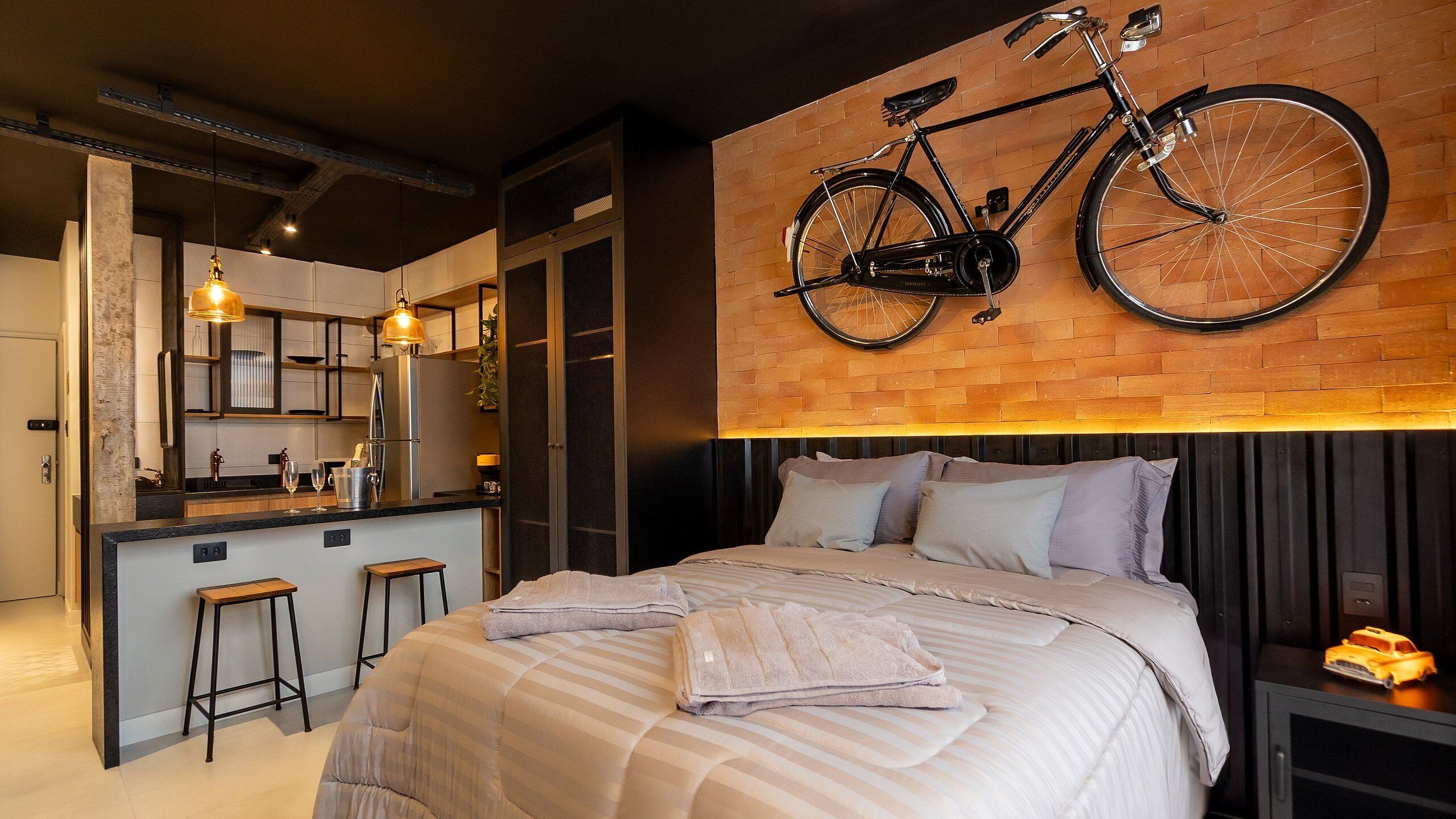 Un dormitorio moderno con una cama grande, una bicicleta colgada en la pared y una cocina visible a través de una puerta abierta.