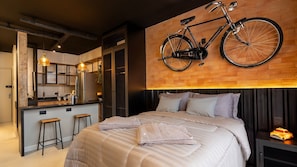 Un dormitorio moderno con una cama grande, una bicicleta colgada en la pared y una cocina visible a través de una puerta abierta.