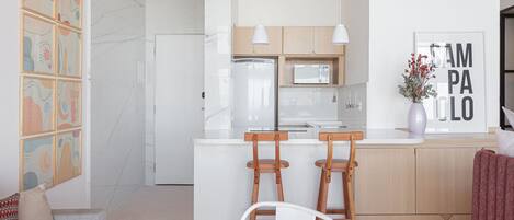 Eine moderne Küche mit weißen Schränken, einer eingebauten Mikrowelle und zwei Holzbarhocker.