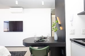 Un comedor moderno con una mesa oscura, paredes blancas y un televisor de pantalla plana montado arriba.
