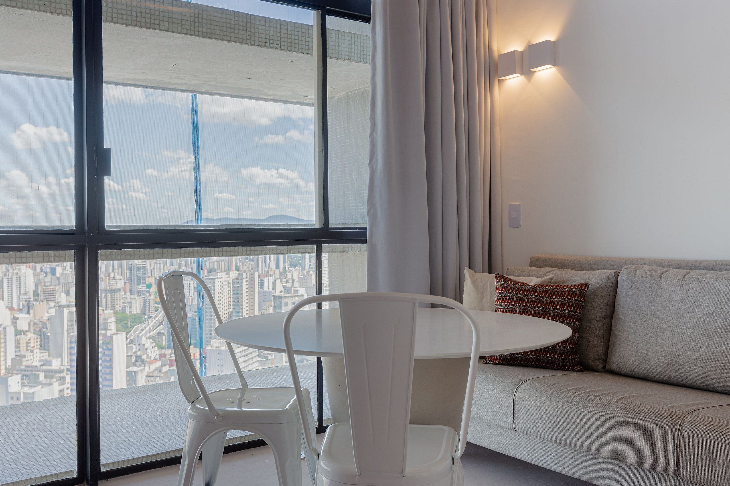 Un saló modern amb vista a la ciutat, un sofà blanc, una taula rodona i una cadira blanca.