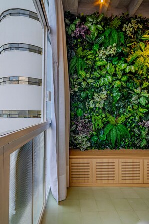 Quarto com uma janela grande, cortina e parede coberta por diversas plantas verdes.