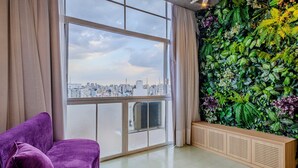 A room with a large window, a purple sofa, and a green wall with plants. - Vossa Bossa Copan (São Paulo)
