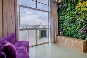 A room with a large window, a purple sofa, and a green wall with plants. - Vossa Bossa Copan (São Paulo)
