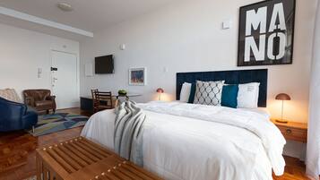 Habitación de hotel con una cama grande, un banco de madera, un escritorio con una silla, un televisor en la pared y una obra de arte enmarcada.