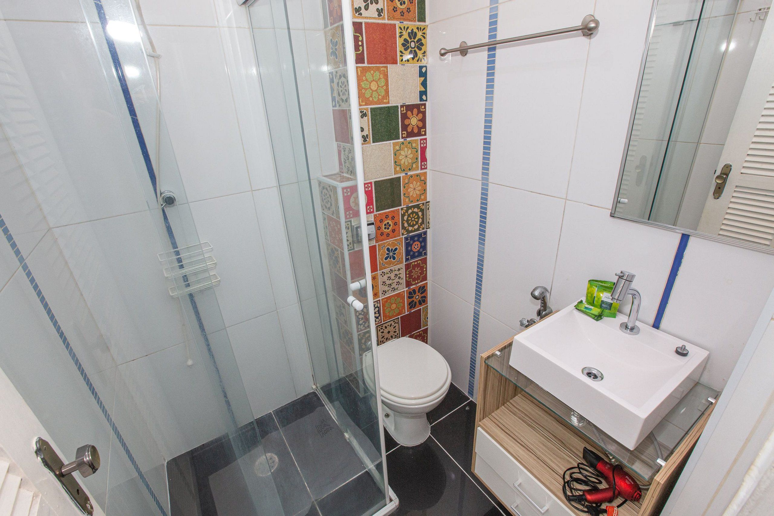 Un baño con cabina de ducha de vidrio, inodoro y lavamanos con espejo.
