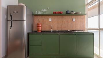 A kitchen with a stainless steel refrigerator, green cabinets, a tiled backsplash, and a window providing natural light.