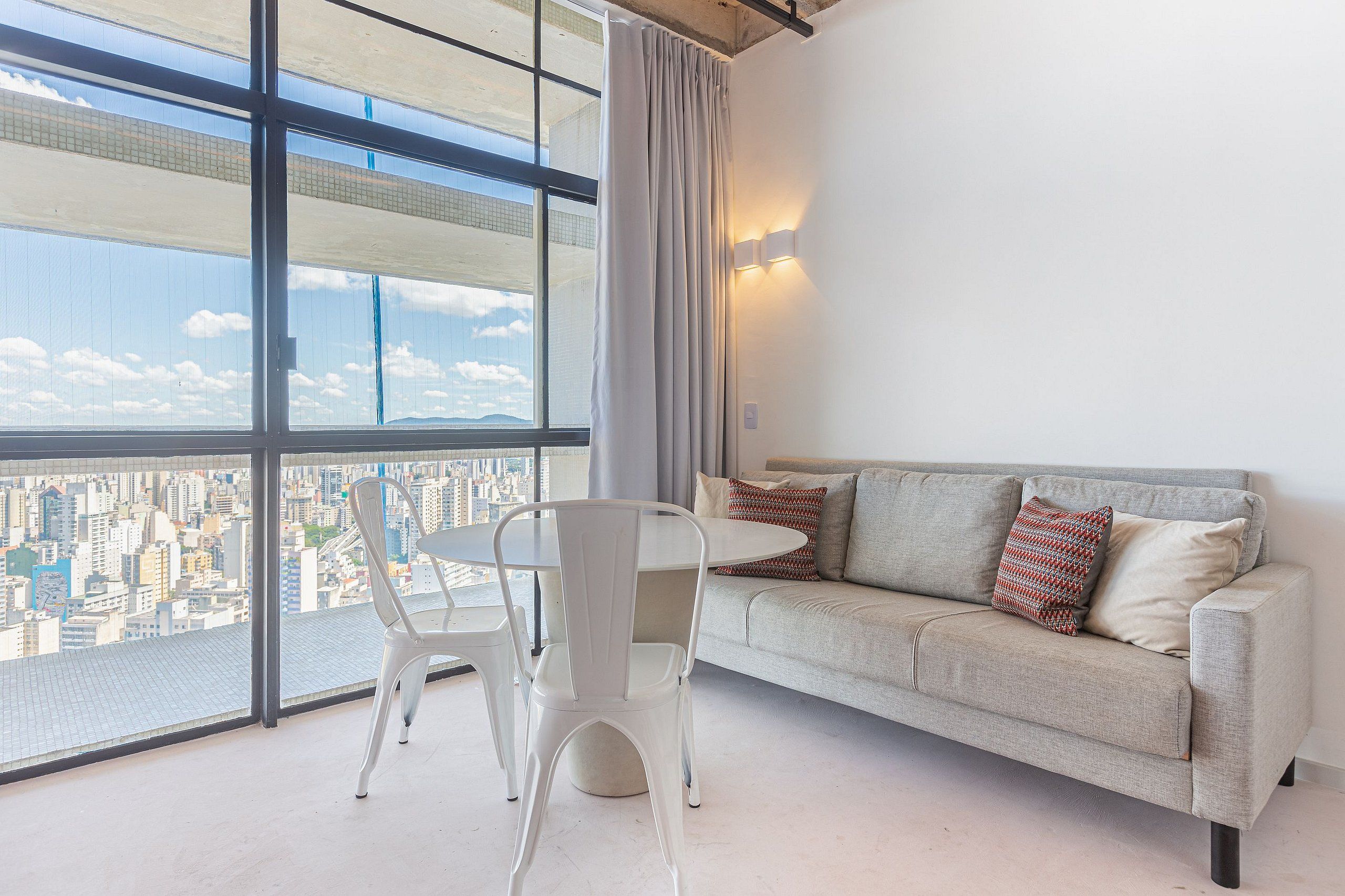 A modern living room with a city view, a sofa, a dining table, and a chair.