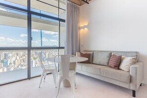 Un salon moderne avec vue sur la ville, comprenant un canapé, une table à manger et un fauteuil.