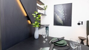 A modern dining area with a dark wooden table, two wine glasses, a vase with a plant, and a framed abstract painting on the wall. - Vossa Bossa Copan (São Paulo)