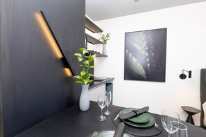 A modern dining area with a dark wooden table, two wine glasses, a vase with a plant, and a framed abstract painting on the wall. - Vossa Bossa Copan (São Paulo)