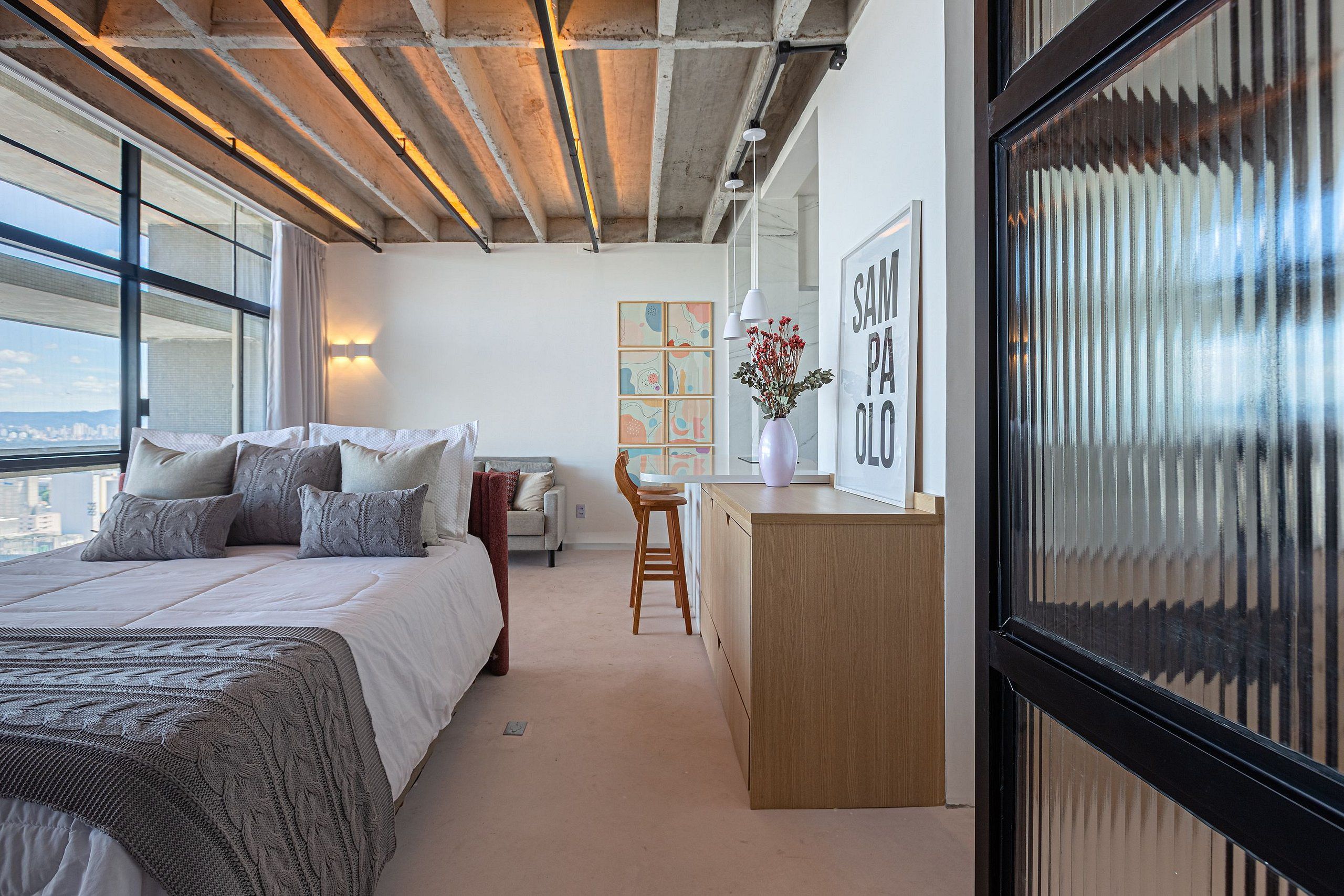 Ein modernes Schlafzimmer mit einem großen Bett, einem Schreibtisch und Blick auf die Stadt.