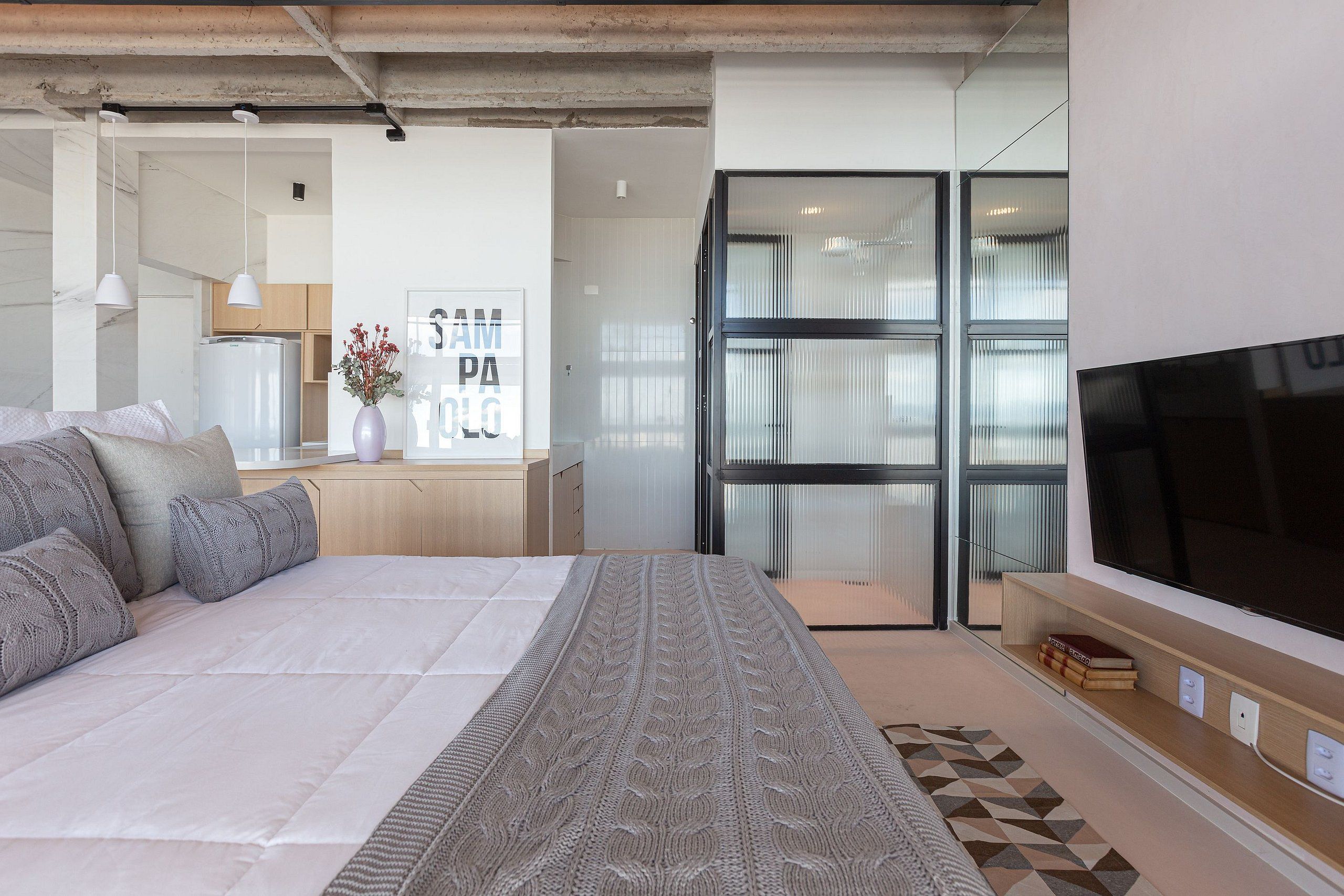 Un dormitorio moderno con una cama grande, televisión y vistas a la cocina.