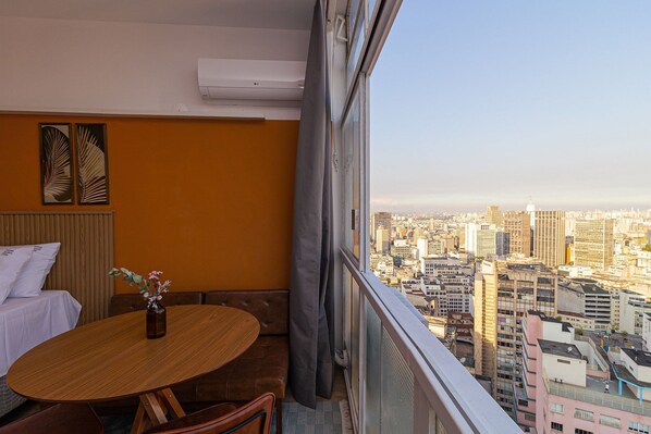 A balcony with a city view, a round wooden table, a vase with flowers, and a white sofa.