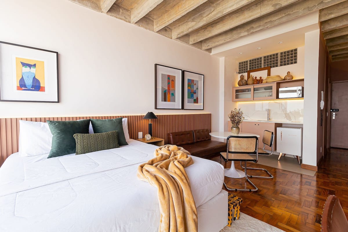 A modern hotel room with a large bed, a desk, and a kitchenette.