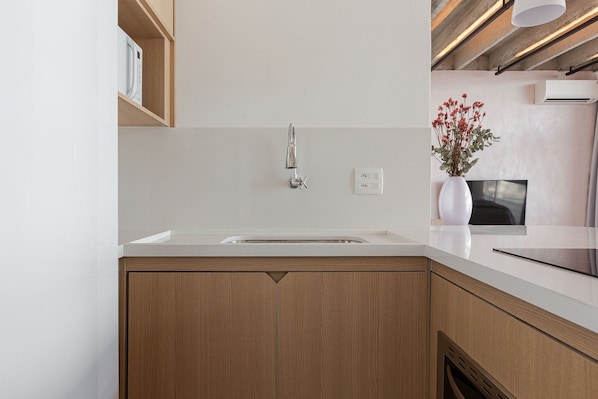 Cozinha moderna com bancada branca, armários de madeira, torneira de aço inoxidável, um vaso branco com flores e um aparelho de ar condicionado na parede.