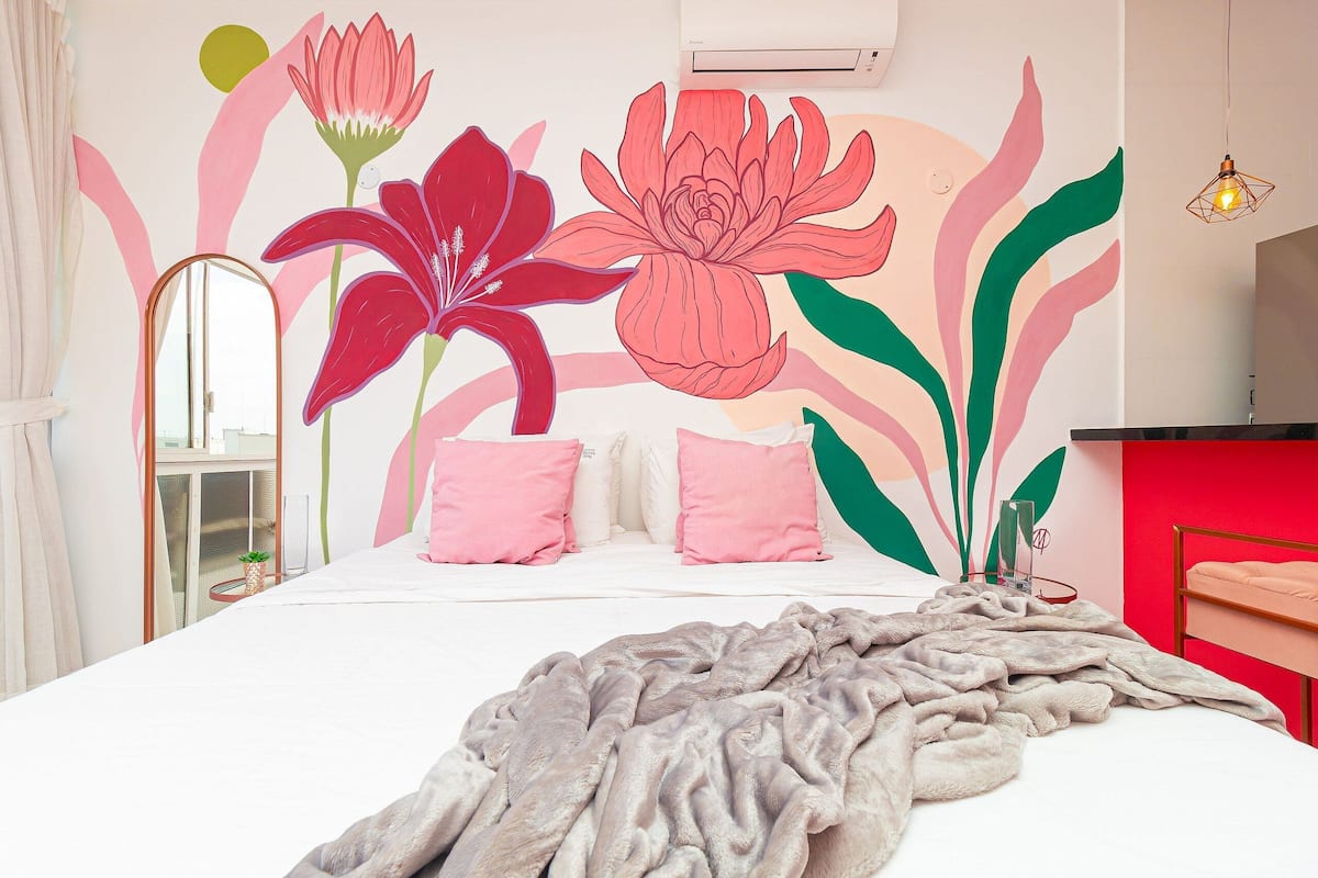A bedroom with a large bed, a mirror, a red wall, and a wall mural of flowers.