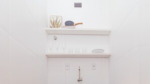 A compact kitchen with white tiles, a wooden cabinet, a red appliance, and a shelf with glasses and a decorative item. - Vossa Bossa Copan (São Paulo)
